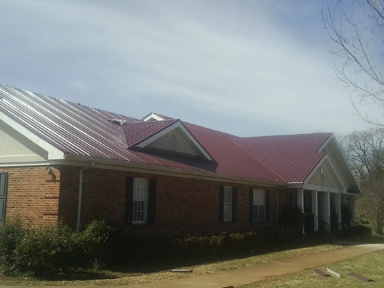 Red metal roof with gabled entries on a long brick building, from a Hail Damage Roof Repair job in Ligonier