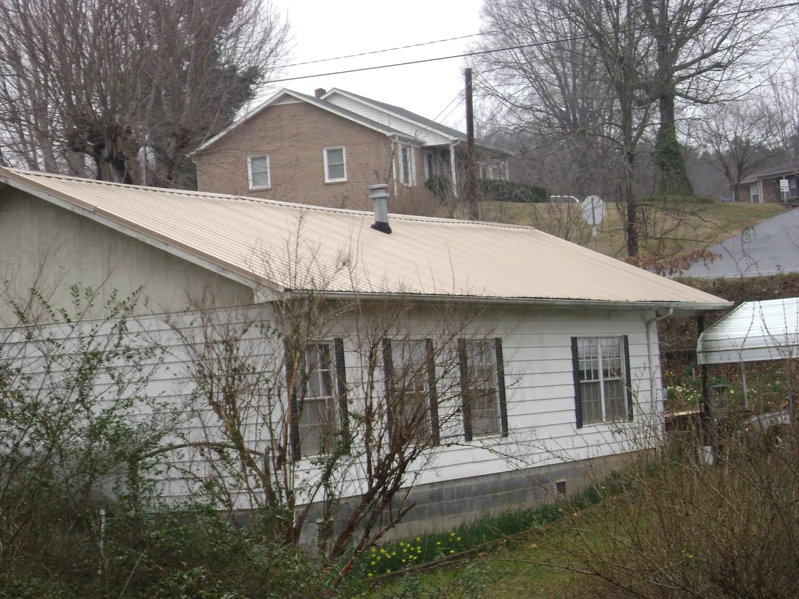 Tan metal roof on a white sided house set into a hillside — Commercial Roofing by Roofing Brothers in Ligonier